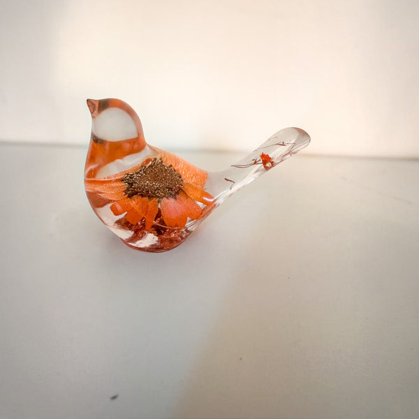 Resin bird decor with orange sunflower encased inside, clear tail featuring small flower accents, and copper leaf base shimmer.