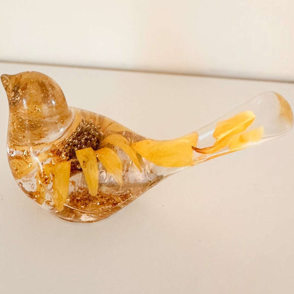 Sunflower resin bird decor with clear body, embedded dried yellow petals, and gold flecks inside for a shimmering effect.