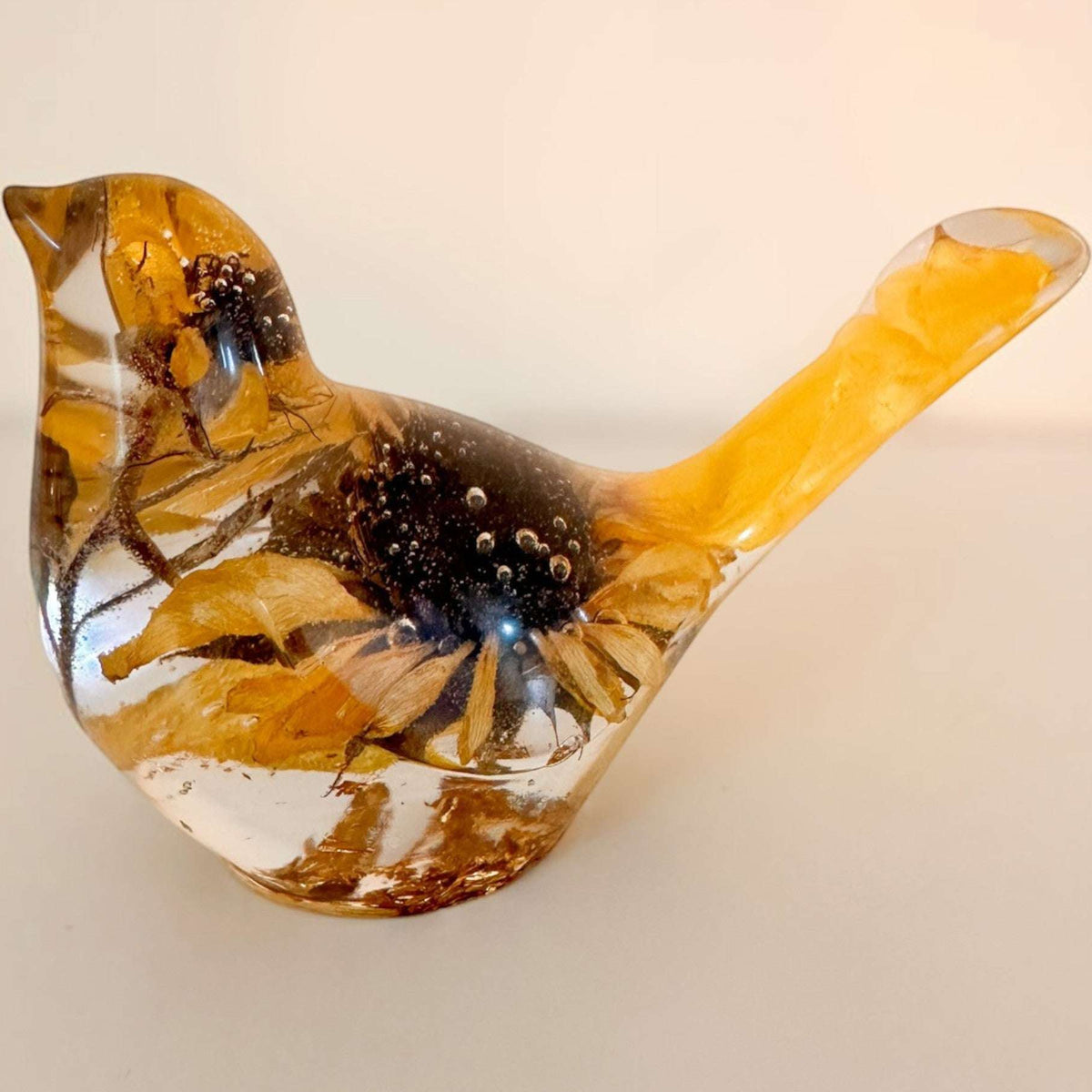 Sunflower resin bird decor in clear material with real dried sunflower petals and golden accents inside a hand-poured form.