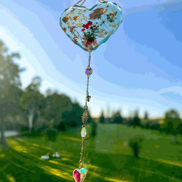 Glow in the dark heart suncatcher in blue resin with real pressed wildflowers, gold chain, and hanging faceted crystal drops.