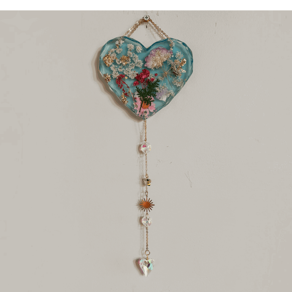 Glow in the dark heart suncatcher handcrafted in blue resin with pressed wildflowers, gold leaf, and decorative gold chain with crystal drops.