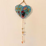 Heart-shaped blue resin glow in the dark heart suncatcher with real pressed wildflowers, gold leaf, and hanging crystal charms.