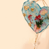 Glow in the dark heart suncatcher in blue resin with real pressed wildflowers, gold leaf accents, and a gold chain with crystal drops.