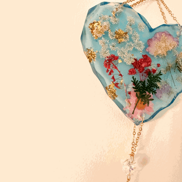 Glow in the dark heart suncatcher in blue resin with real pressed wildflowers, gold leaf accents, and a gold chain with crystal drops.