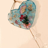 Blue resin glow in the dark heart suncatcher with real pressed wildflowers, gold leaf accents, and a gold chain with crystal drops.