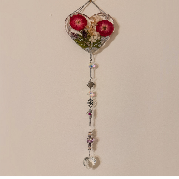 Pressed rose suncatcher featuring two deep crimson roses in clear resin with silver leaf, hanging silver chain with crystal prisms, sunburst, leaf, and hummingbird charms.