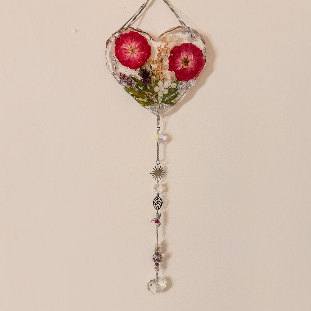 Heart-shaped pressed rose suncatcher with two deep pink roses, green leaves, silver chain, crystal prisms, and charms hanging below