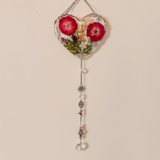 Heart-shaped pressed rose suncatcher with two deep pink roses, green leaves, silver chain, crystal prisms, and charms hanging below