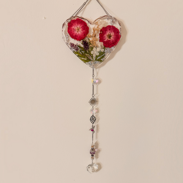 Heart-shaped pressed rose suncatcher with two deep pink roses, green leaves, silver chain, crystal prisms, and charms hanging below
