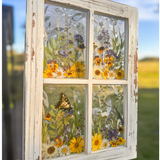 Pressed Flower Window Frame with white distressed wood, clear resin panes containing real dried yellow, white, and purple wildflowers, butterflies, and intricate holographic patterns behind each pane.