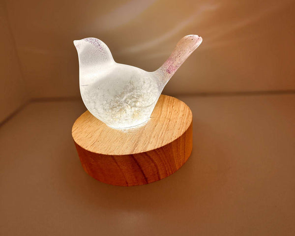Glow in the Dark Resin Bird, milky white with violet glitter and a translucent dandelion puff, on a wood base