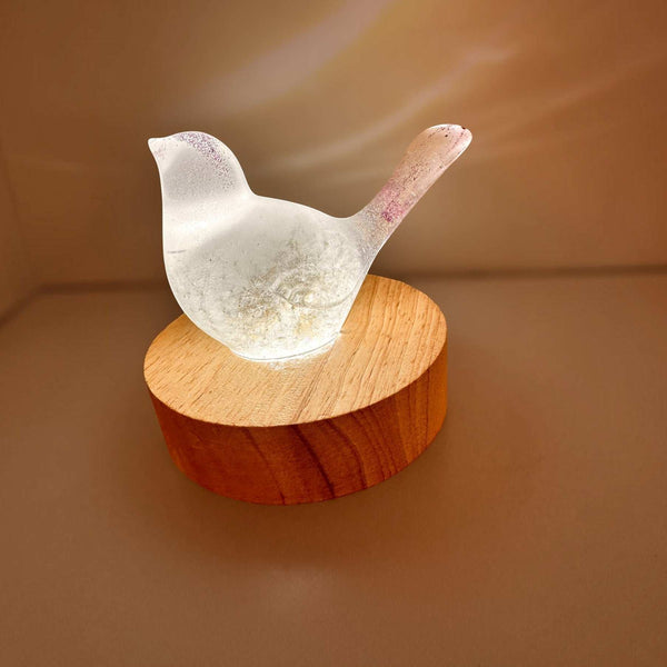 Glow in the Dark Resin Bird, milky white with violet glitter and a translucent dandelion puff, on a wood base