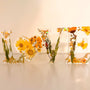 Pressed flower resin love sign in clear resin, featuring yellow wildflowers, greenery, and a floral heart-shaped O