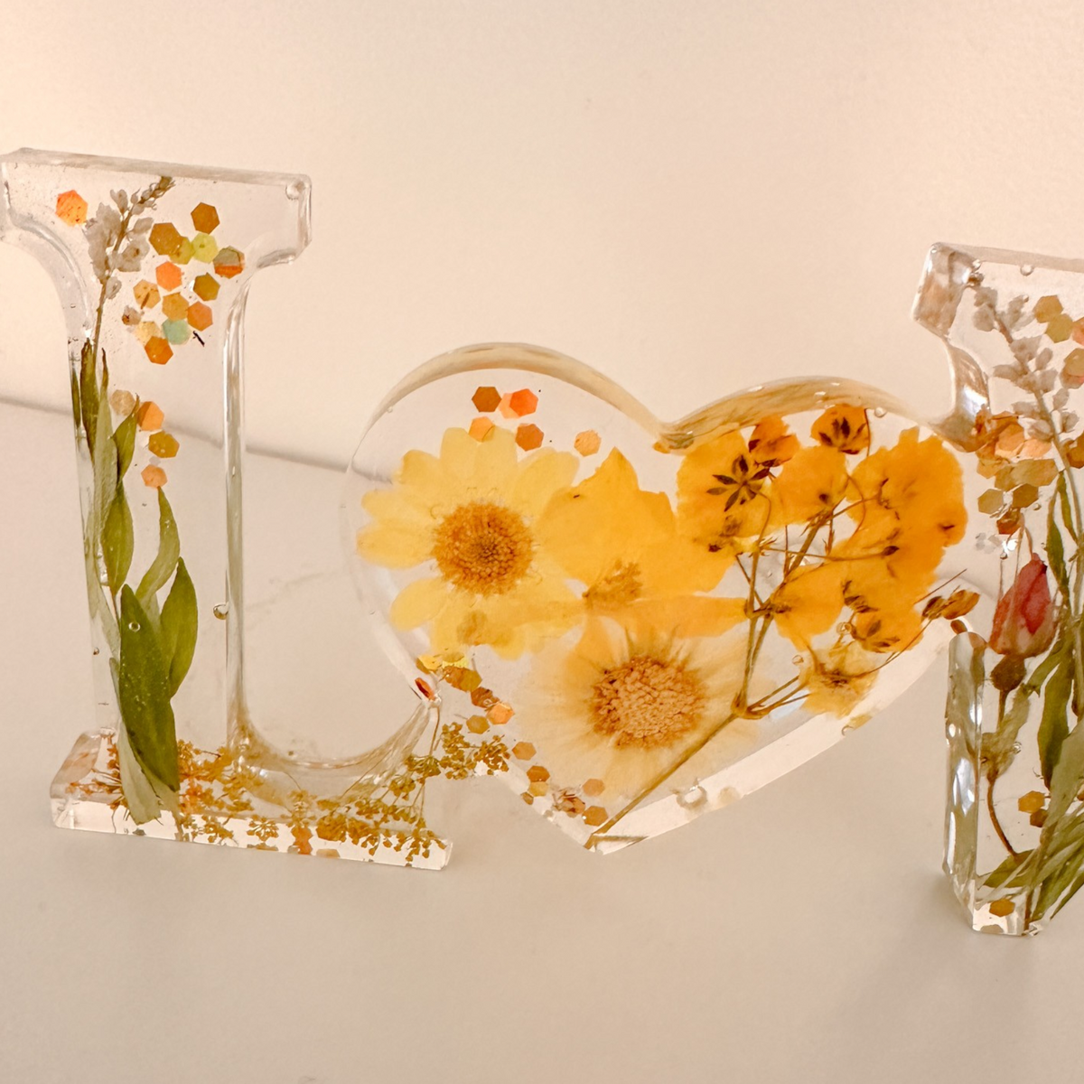 Pressed flower resin love sign in clear resin with yellow wildflowers and a heart-shaped O centerpiece