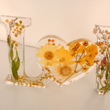 Pressed flower resin love sign in clear resin with yellow wildflowers and a heart-shaped O centerpiece