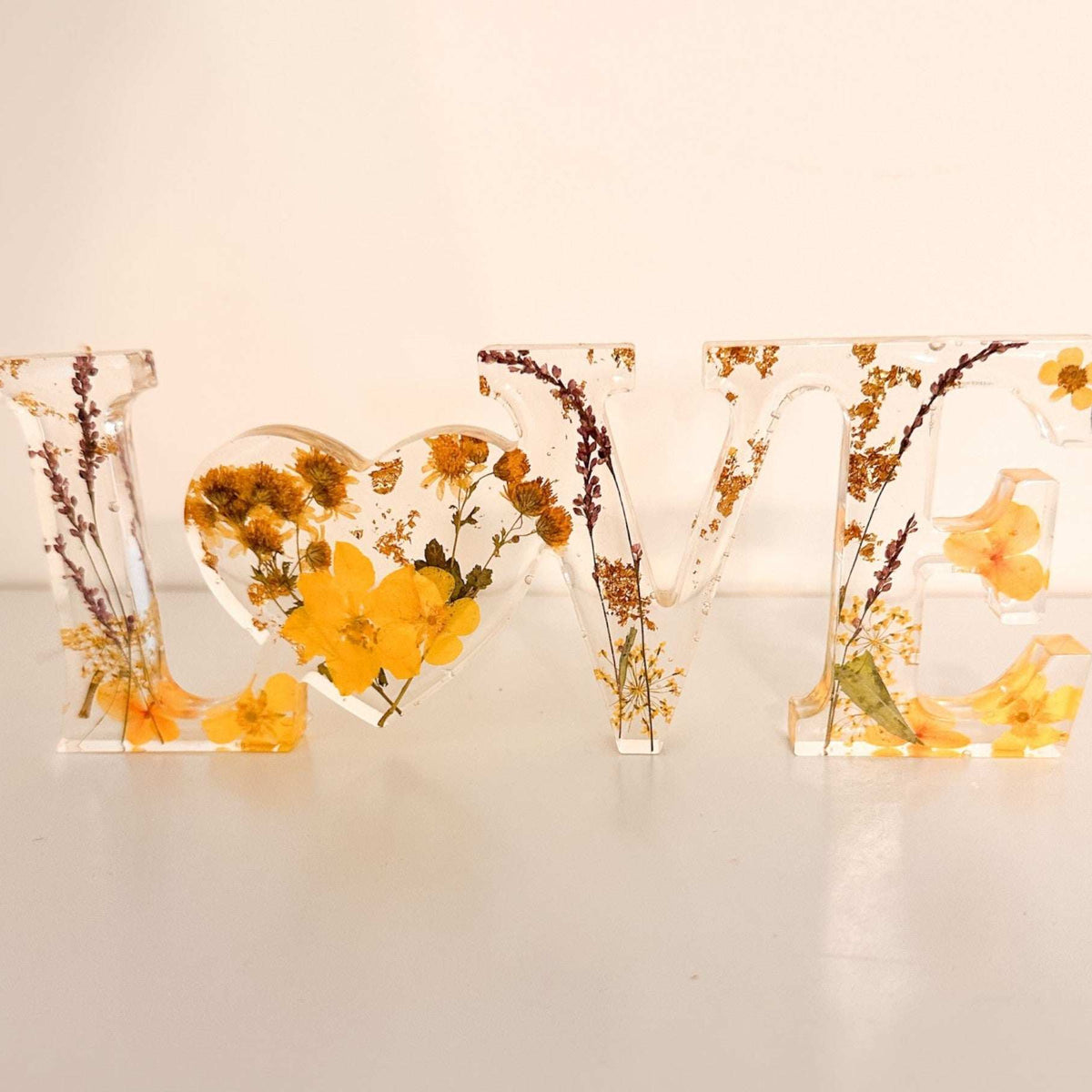 Pressed flower resin love sign in clear resin with yellow wildflowers, greenery, and a heart-shaped O centerpiece