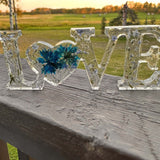forget me not resin love sign in clear resin with blue pressed flowers, silver leaf flakes and heart-shaped O