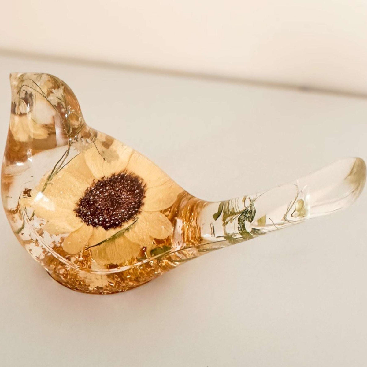 Resin bird decor with a pressed Sunflower, golden-brown tones, delicate green botanicals, and a clear glossy finish.