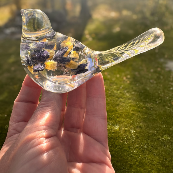 Blue Lupine resin bird decor in clear resin with embedded dark blue and yellow botanicals and a slender, leafy tail.