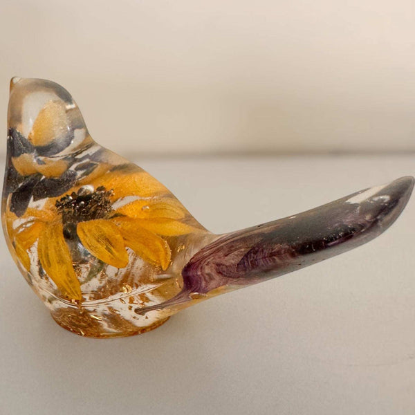 Sunflower lupine resin bird decor, clear handcrafted bird with golden sunflower petals, dark seeds, and plum-purple tail petals.