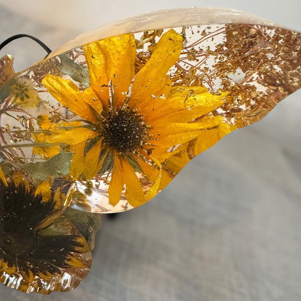 Light up resin butterfly decor with clear resin wings, pressed golden sunflowers, dark centers, green leaves and gold flecks.