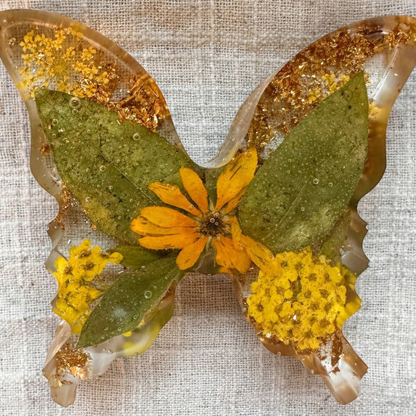 Light up resin butterfly decor in clear resin with green leaves, yellow flowers, orange petals, and gold leaf