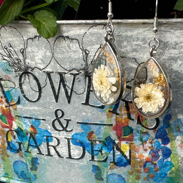 A teardrop silver frame is filled with real dried white flowers and flakes of gold foil are a romantic set of earrings