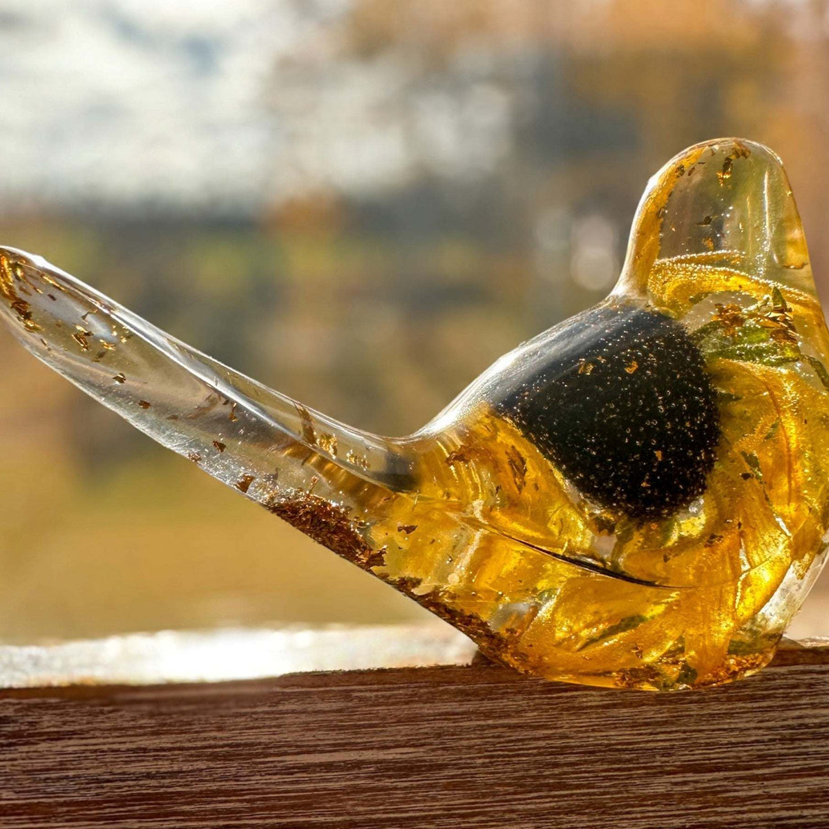 Resin bird in clear amber-gold resin with a preserved yellow flower and dark centre; Golden Meadow design with gold flecks.