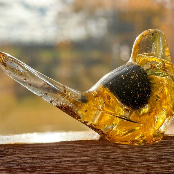Resin bird in clear amber-gold resin with a preserved yellow flower and dark centre; Golden Meadow design with gold flecks.