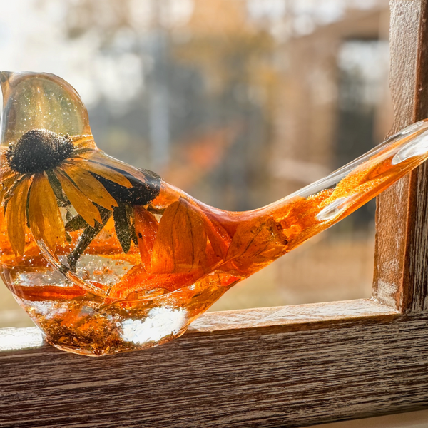 Resin bird in clear amber-tinted resin with a preserved golden flower and black centre, flecks of gold leaf; Golden Meadow decor.