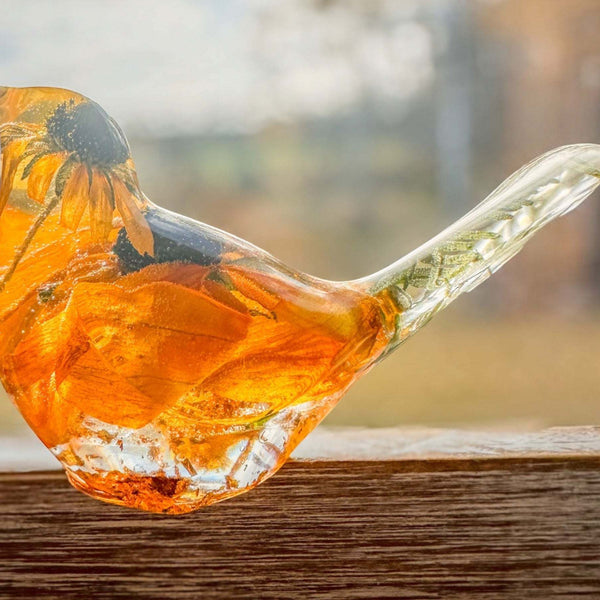 Resin bird ornament in clear resin with vivid orange and yellow preserved flower petals, a dark centre and clear tail; Golden Meadow design.
