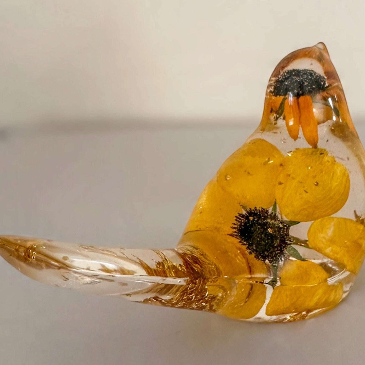 Golden Meadow resin bird with clear glossy body, preserved yellow black-eyed susan blooms and dark centres, plus gold accents.
