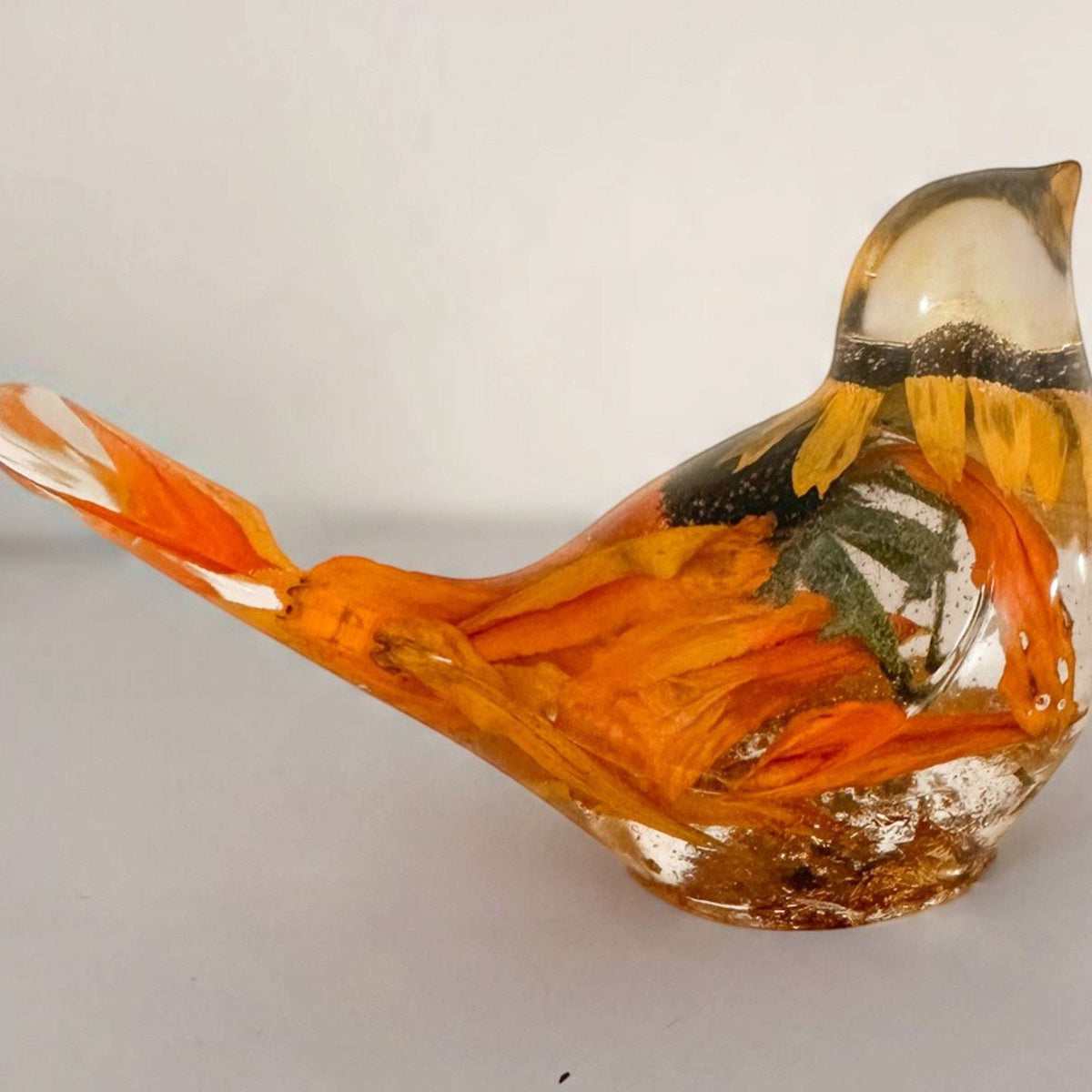 Golden Meadow resin bird with a clear glossy body, orange and gold botanical details, and a curved tail and crest.