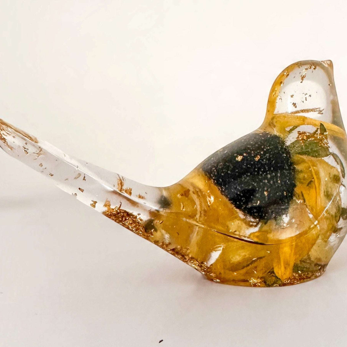 Resin bird with a preserved yellow bloom and dark centre, clear glossy finish, and gold leaf accents; Golden Meadow décor