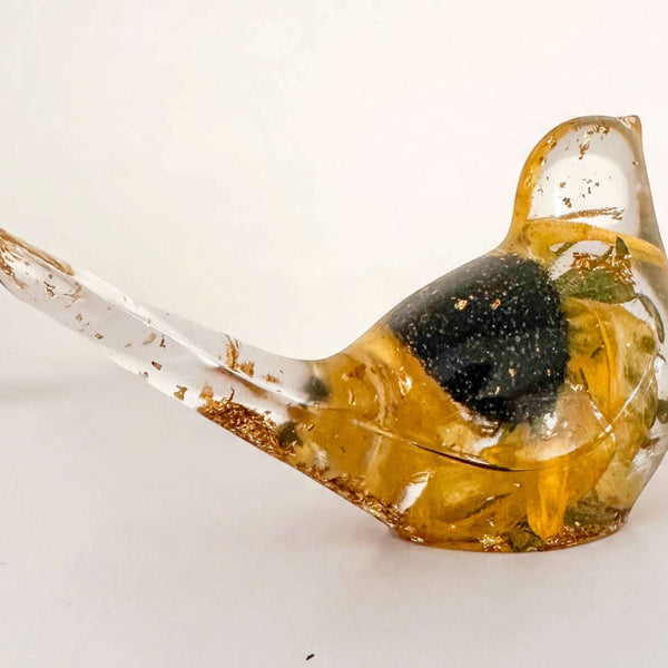 Resin bird with a preserved yellow bloom and dark centre, clear glossy finish, and gold leaf accents; Golden Meadow décor