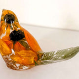 Resin bird with orange and yellow preserved blooms, dark centers and a clear greenish tail; Golden Meadow botanical decor