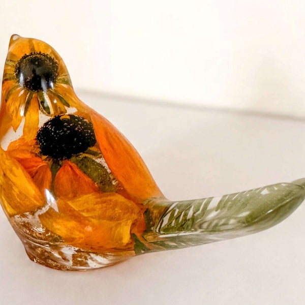 Resin bird with orange and yellow preserved blooms, dark centers and a clear greenish tail; Golden Meadow botanical decor