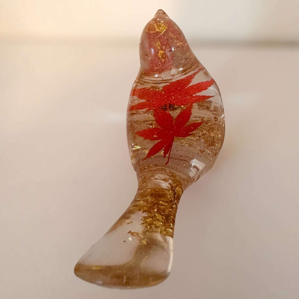 Maple Leaf Songbird in clear amber resin, featuring a vivid red maple leaf and shimmering gold flecks.