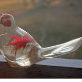 Maple Leaf Songbird in clear resin, with a suspended red maple leaf and subtle gold flecks, handmade with a curved tail.