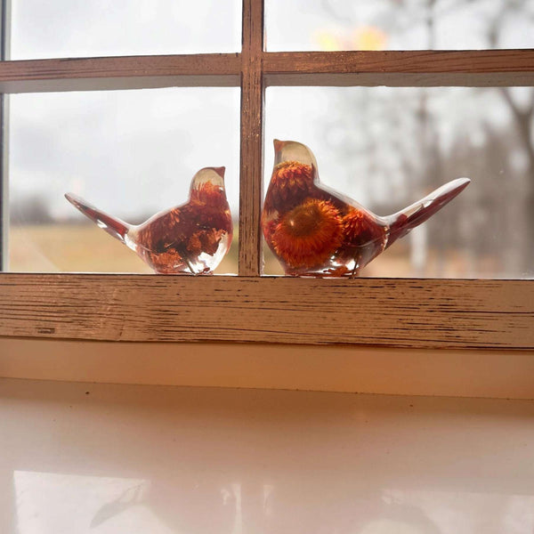 Resin Bird Pair of two clear resin birds with copper-toned bases, red and orange dried flowers, and pointed tails.