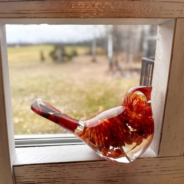 Resin Bird Pair featuring a transparent amber-red bird with embedded dried flowers and botanicals in its body and tail.