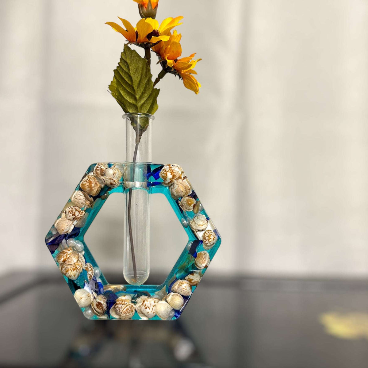 A hexagon shaped propergation bud vase created with Epoxy Resin. The first layer is filled with real seashells, the background layer is a bright teal blue. Comes with a test tube that will hold your favourite flower or plant you wish to start and root