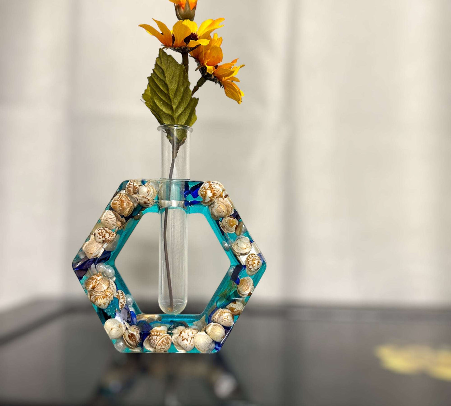 A hexagon shaped propergation bud vase created with Epoxy Resin. The first layer is filled with real seashells, the background layer is a bright teal blue. Comes with a test tube that will hold your favourite flower or plant you wish to start and root