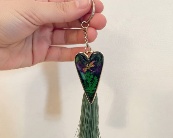 Aurora dragonfly keychain with a silver heart frame, dark green and purple resin, fern pattern, dragonfly and green tassel.