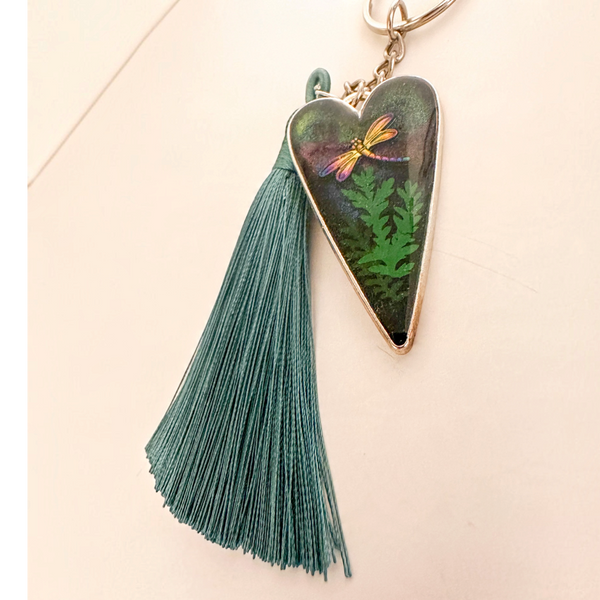Aurora dragonfly keychain with a silver heart frame, green ferns in glossy resin, colourful dragonfly and teal tassel.