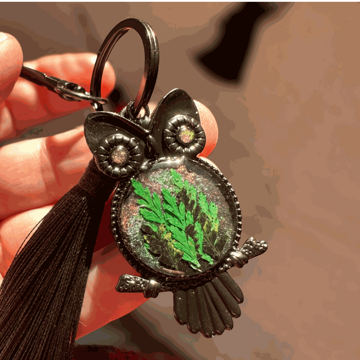 Bag Charm featuring a dark gunmetal owl frame, green pressed ferns in shimmering resin, jeweled eyes and black tassel