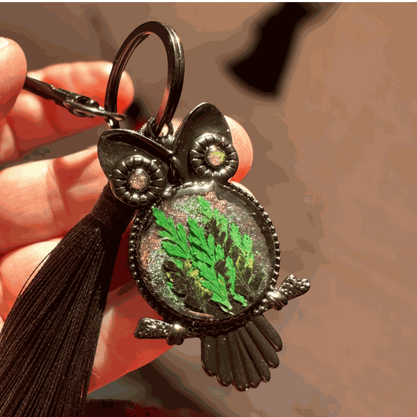 Bag Charm featuring a dark gunmetal owl frame, green pressed ferns in shimmering resin, jeweled eyes and black tassel
