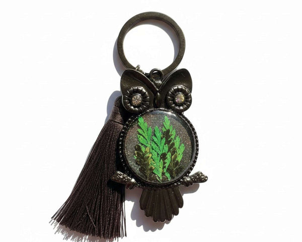 Bag Charm featuring a dark gunmetal owl with sparkling eyes, bright green fern in shimmering resin, and black tassel