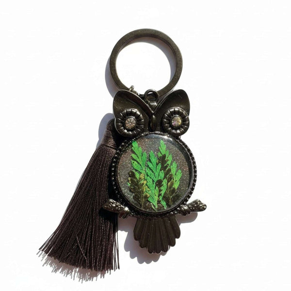 Bag Charm featuring a dark gunmetal owl with sparkling eyes, bright green fern in shimmering resin, and black tassel