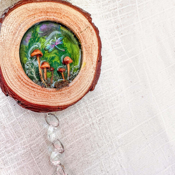 boreal forest suncatcher in a natural bark-edged wood slice, with green resin, tiny mushrooms, moss, dragonfly and hanging crystals